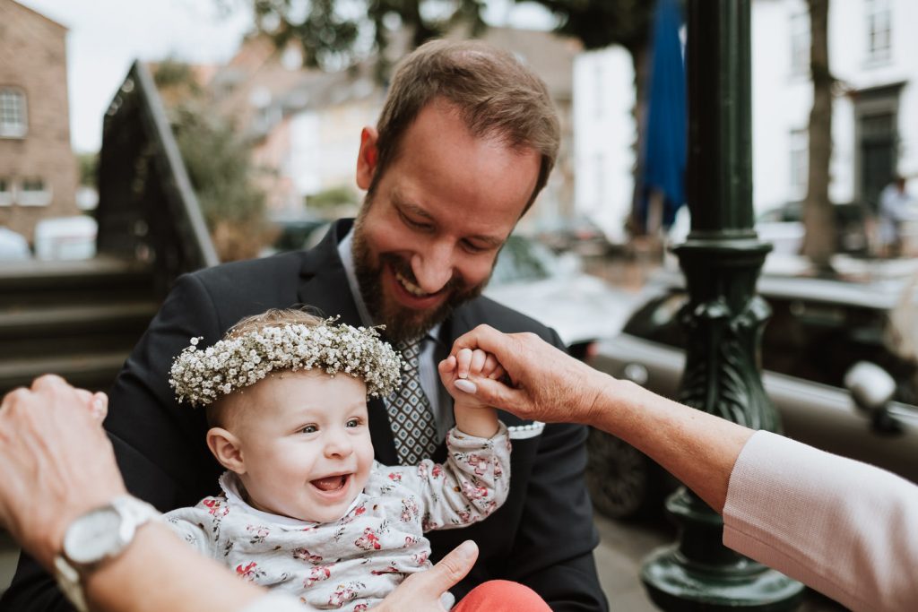 Bräutigam hat seine kleine Tochter auf dem Arm, die mit der Oma spielt