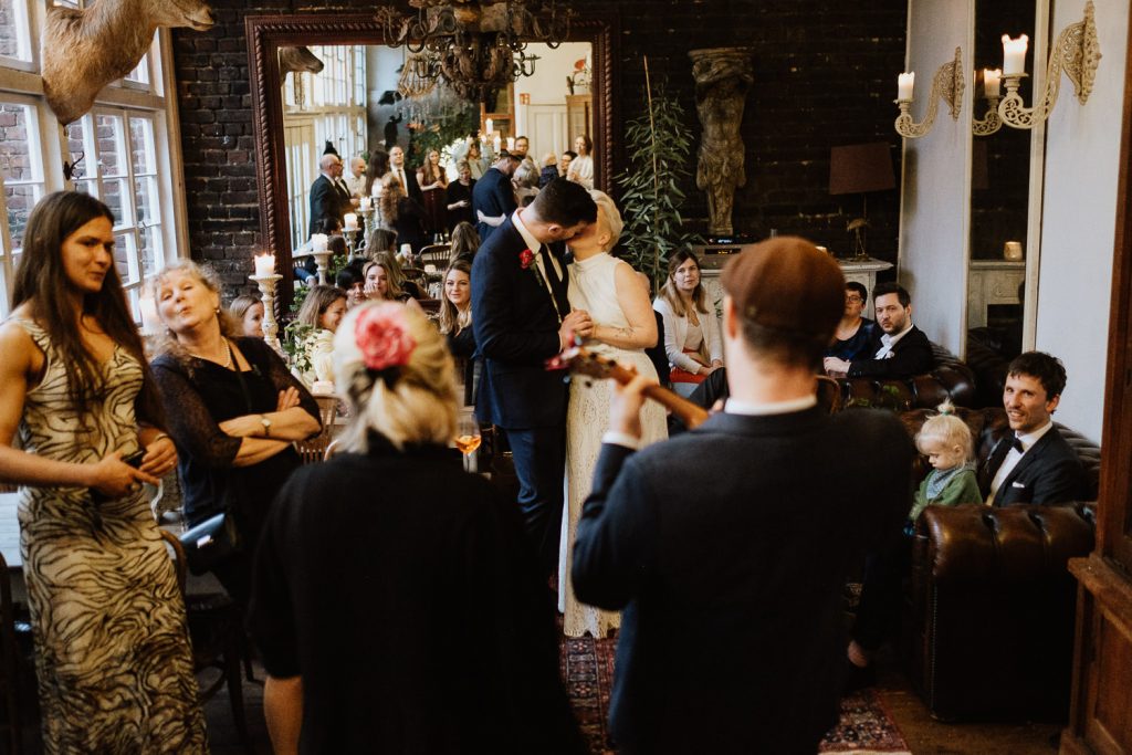 Brautpaar küsst sich vor den Gästen während ein Gast Ukulele spielt