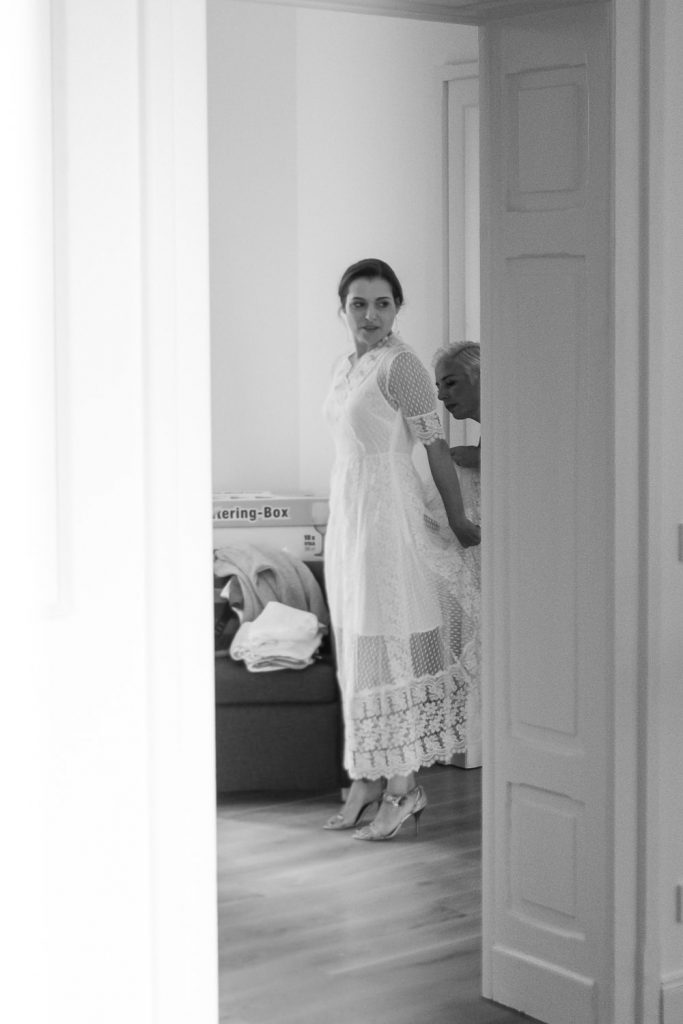 Braut zieht sich das Brautkleid mit Hilfe ihrer Trauzeugin vor dem Spiegel an