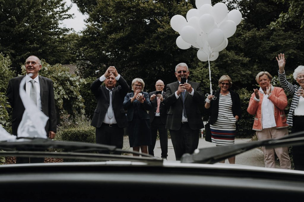 Hochzeitsgesellschaft fotografiert das wegfahrende Hochzeitsauto