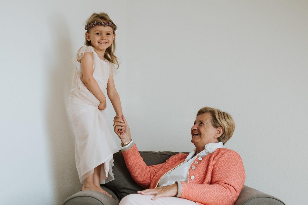Oma und Blumenmädchen einer Hochzeit spielen zusammen auf einem Sessel