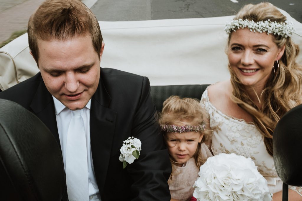 Brautpaar und kleine Tochter sitzen gemeinsam auf der Rückbank eines Autos