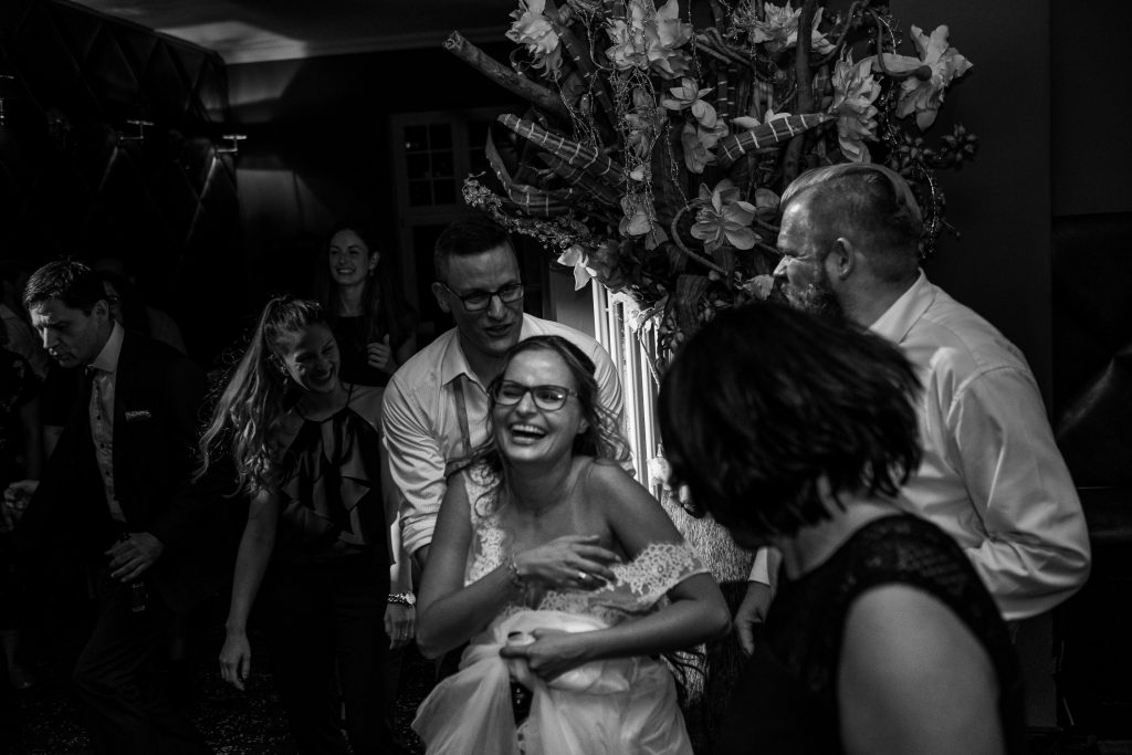 Braut lacht herzlich auf der Tanzfläche weil hr das Kleid von der Schulter rutscht